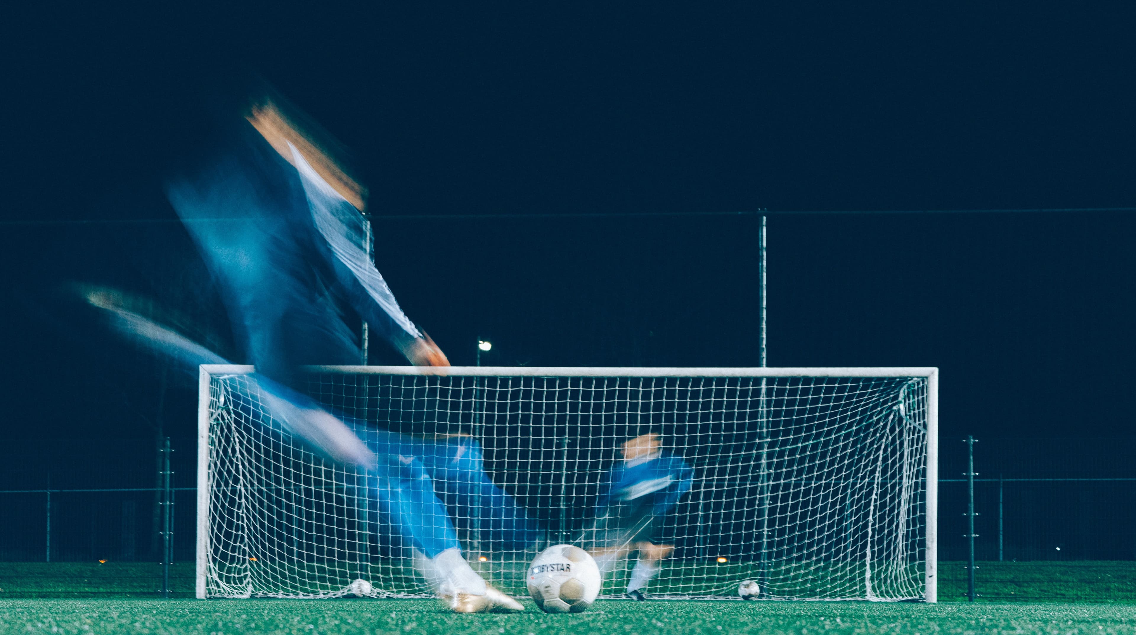 Soccer player taking a shot on goal under stadium lights at night